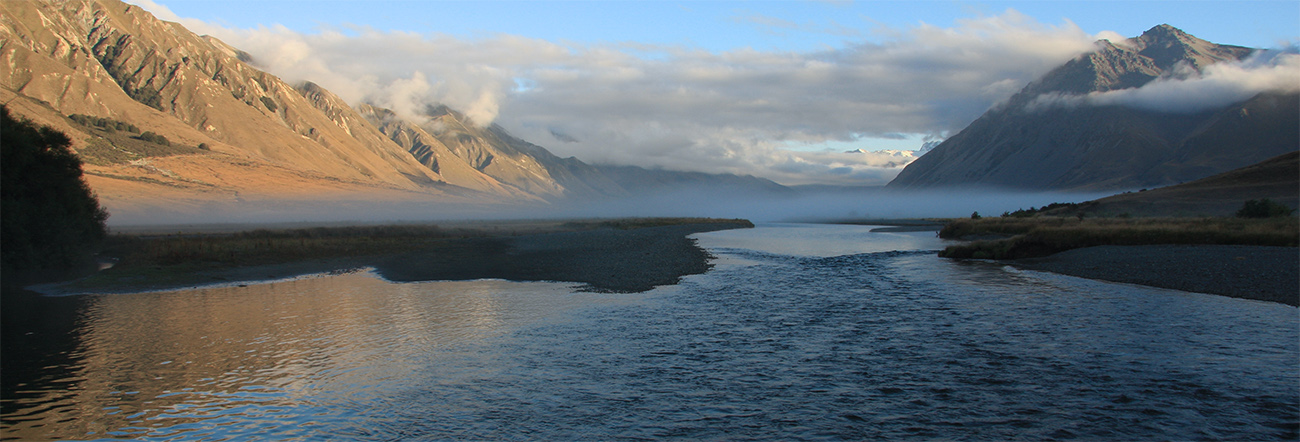 Ahuriri River, South Island, New Zealand, at daybreak with mist hanging over the water and left mountains illumined by rising sun