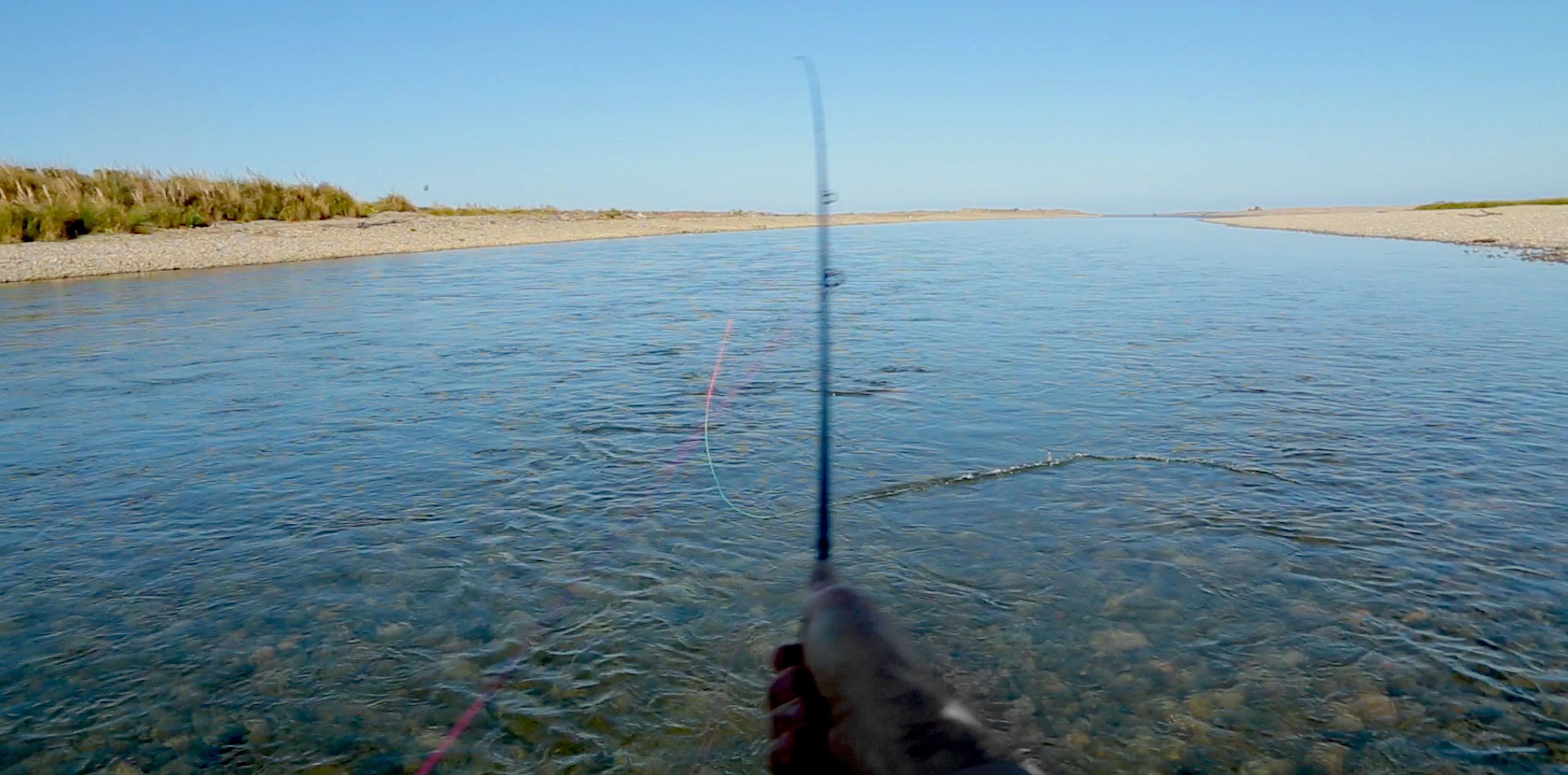 Rod in Spey casting action on wide river, photographed from behind fisherman