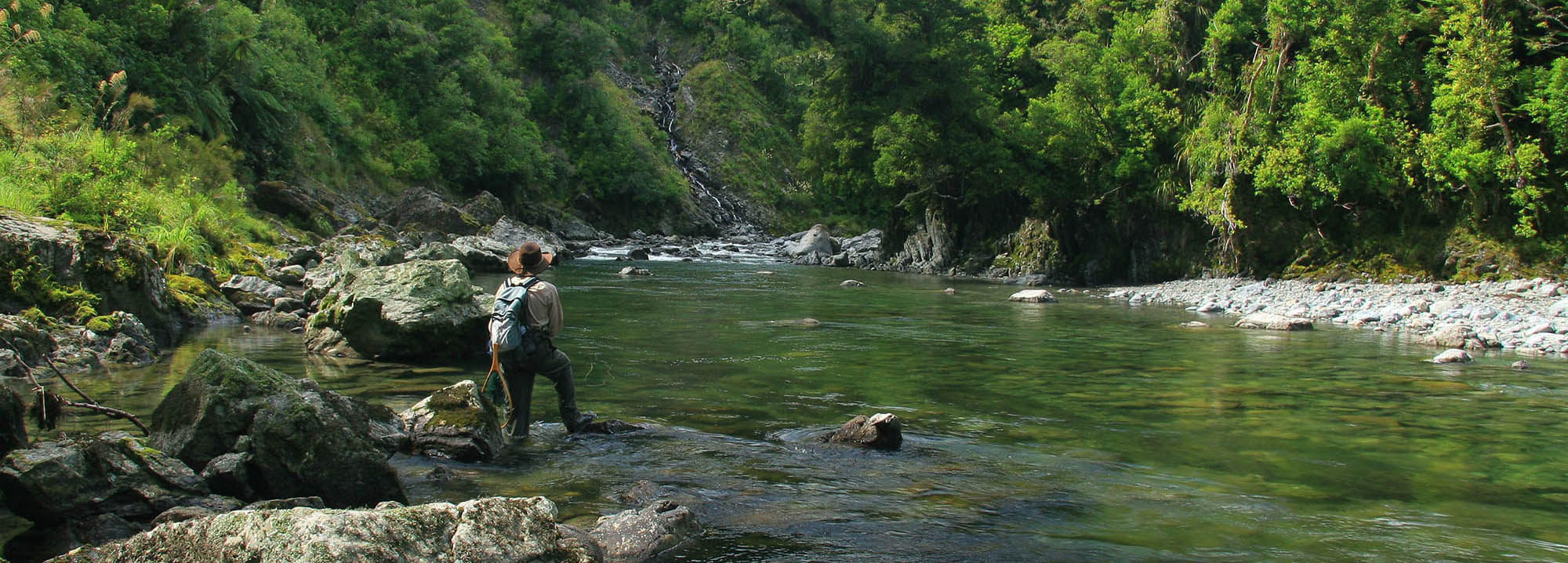 Fisherman stands contemplating a wide, wild and beautiful backcountry river in New Zealand