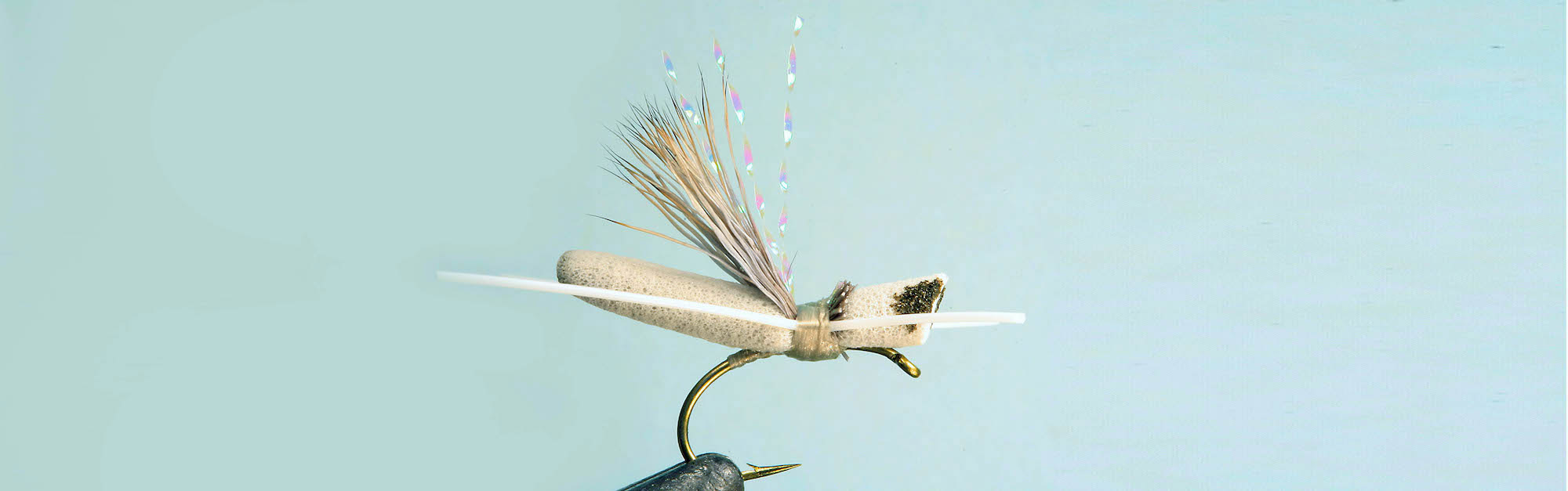 Close up of Hot Foam Hopper Fly in a vise on a pale greenish-blue background