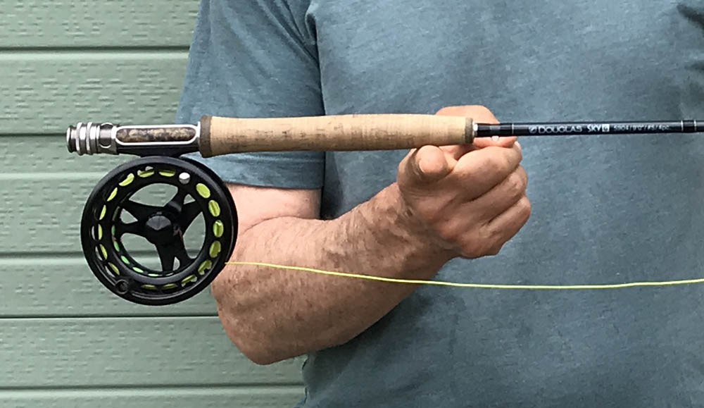 Man balancing a rod on his finger to find ideal balancing with a green garage door behind him