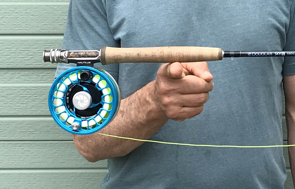 Man in a blue shirt balancing a rod with a reel on his finger with a green garage door behind him