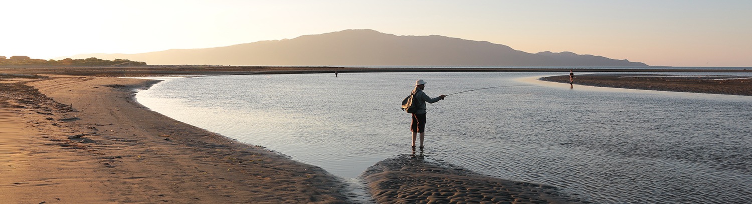 Fly fisherman trout spey casting on estuary at dusk