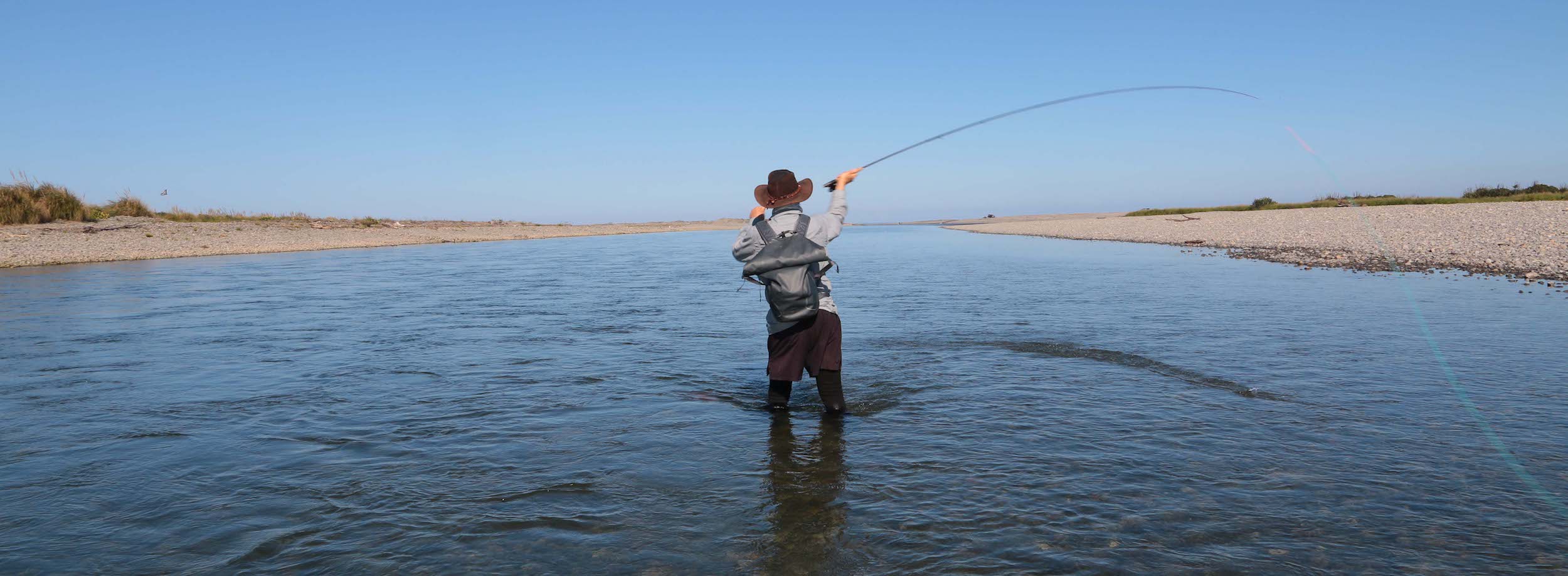 Fly fisherman, from behind, standing Spey casting in wide river mouth, using single-hand Spey rod, skagit head, line and sink tip