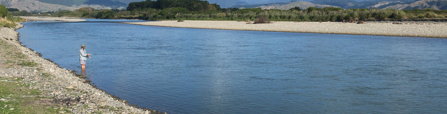 Fly fisherman spey casting on wide river with mountains in background and blue sky
