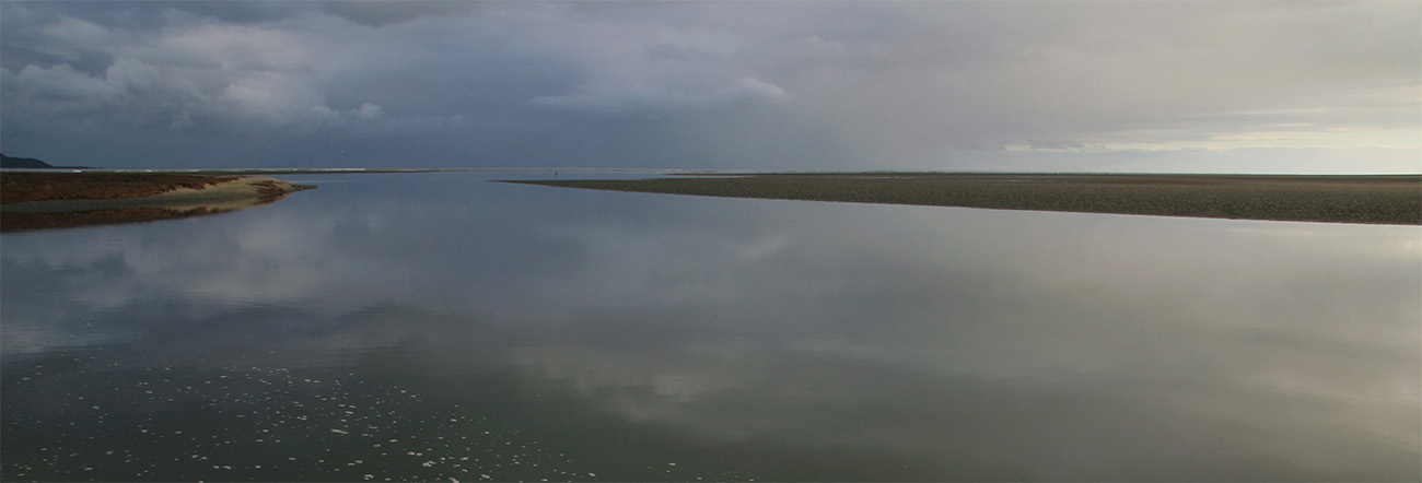 Very calm estuary before first light, muted tones of sky reflected on water's surface